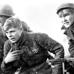 Two men of the 82nd Airborne Division bringing in a young German SS Trooper captured while on reconnaissance patrol during the Battle of the Bulge, 1944