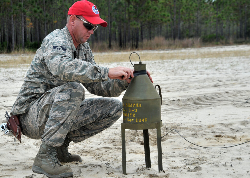 T/Sgt Joseph Dwan, 823rd RED HORSE Squadron heavy equipment and construction supervisor, tapes detonating cord to the top of a shaped charge at the explosive ordnance disposal range on Hurlburt Field, Fla., Nov. 21, 2013. The shaped charges made initial holes in the ground by directing the force of the explosion downward. (US Air Force photo/Senior Airman Kentavist P. Brackin)