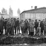 Group_portrait_of_survivors_standing_by_moat_at_dachau_camp