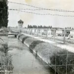 View of the moat, barbed wire and one of the guard towers of the concentration camp at Dachau, 1945