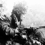 002 – Camouflaged German paratrooper with automatic rifle FG 42 in battle of the hedgerows, Normandy 1944 (Bundesarchiv)