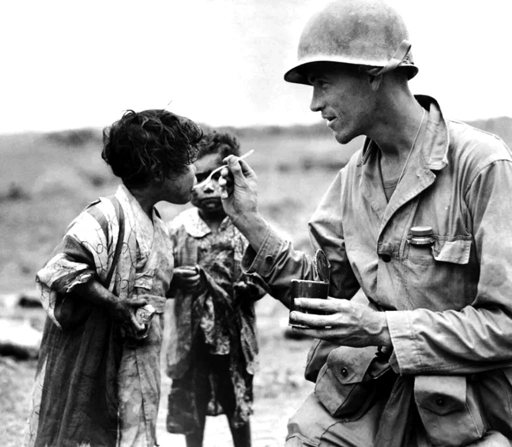 An American serviceman shares his rations with two Japanese children. Okinawa, 1945