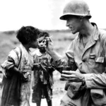 An American serviceman shares his rations with two Japanese children. Okinawa, 1945