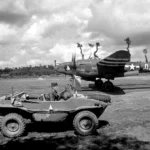 A pilot driving past a P-38 Lightning in a captured German Schwimmwagen at Cricqueville in August 1944