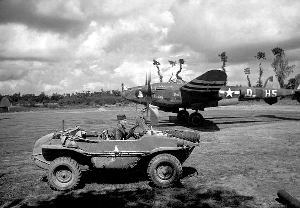 A pilot driving past a P-38 Lightning in a captured German Schwimmwagen at Cricqueville in August 1944