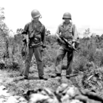 Two members of the 5307 (C)(P) Merrill’s Marauders and their M-1928-A1 .45 Cal Thompson SMGs look at two fallen enemy soldiers at Myitkyina Airfield in Burma – May 1944