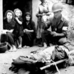 2-AD-EUCMH-Operation Husky-Sicily-1943-Sicily was dirty, poverty-stricken and dangerous. A medic of the 3-ID tends to an injured soldier while four generations of a barefoot Sicilian family watches.