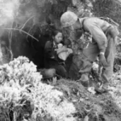A woman holding a baby emerges from a cave during the Battle of Okinawa in 1945