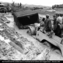 Army trucks, stuck in impassable mud, wait to be pulled out by a bulldozer