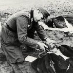 Ein Wehrmachtssoldat zeigt in Nemmersdorf der Kamera eines Kriegsberichterstatters die Leiche eines getöteten Zivilisten