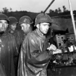 Grim-faced American soldiers fight listen to the radio broadcast of the surrender of Germany and the end of the war in Europe