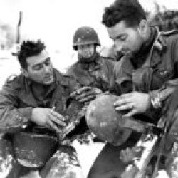 S-Sgt Minicozzi and Pfc Masiero 1-290-IR 75-ID examine a helmet & liner pierced by an enemy bullet which drew blood from the temple of Pfc Masiero during the Battle of the Bulge
