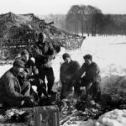 The crew of a Self-Propelled 105-MM Howitzer keep warm around a fire, between the fire missions near Les Tailles, Belgium